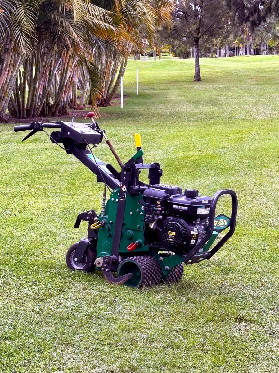 Ryan Jr. Sod Cutter sobre césped de campo de golf con palmeras al fondo